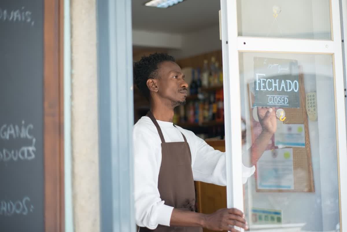 A small business owner in an apron holding a sign outside their shop